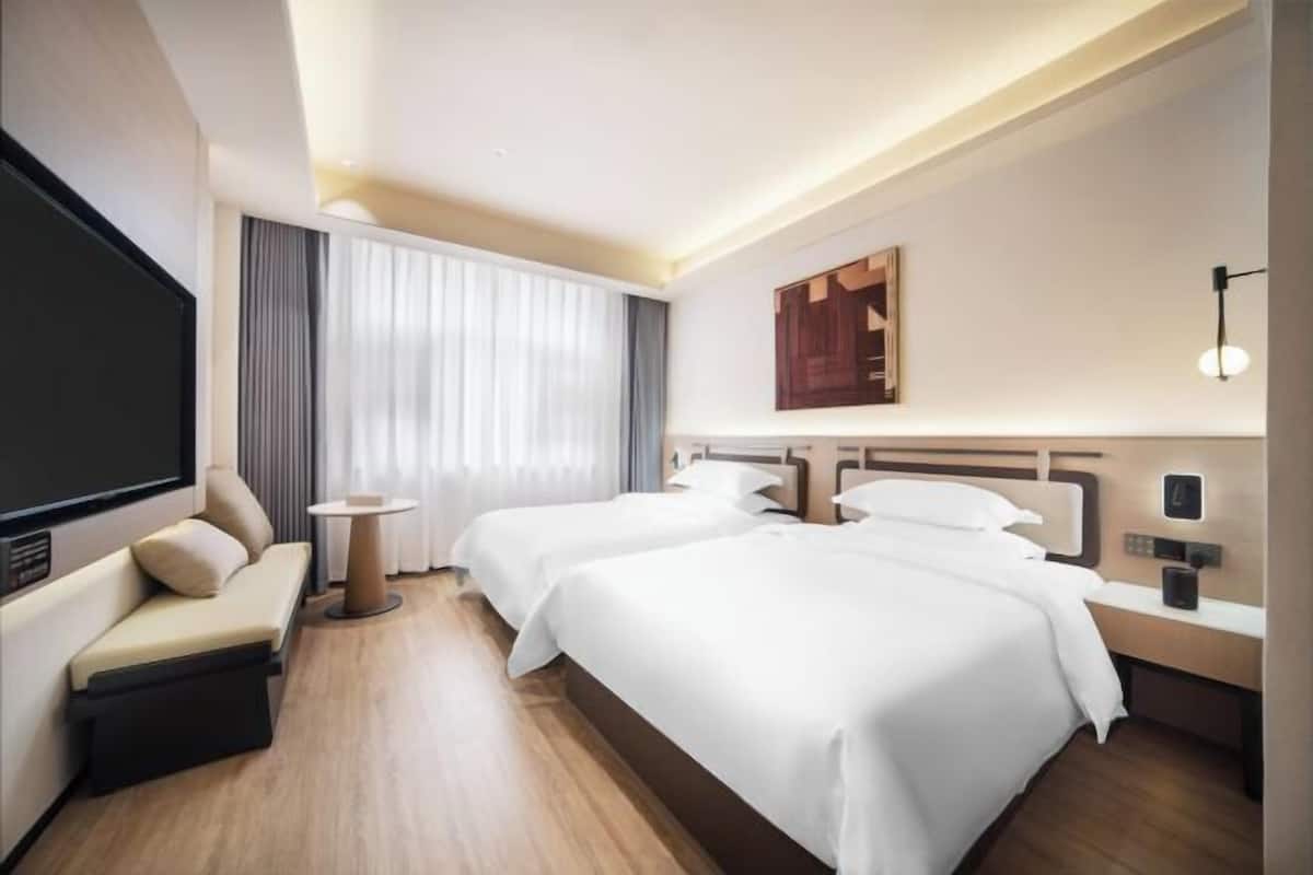 Ein Hotelzimmer mit zwei Betten, einem Schlafsofa, einem Fernseher und einem großen Fenster mit Vorhängen.