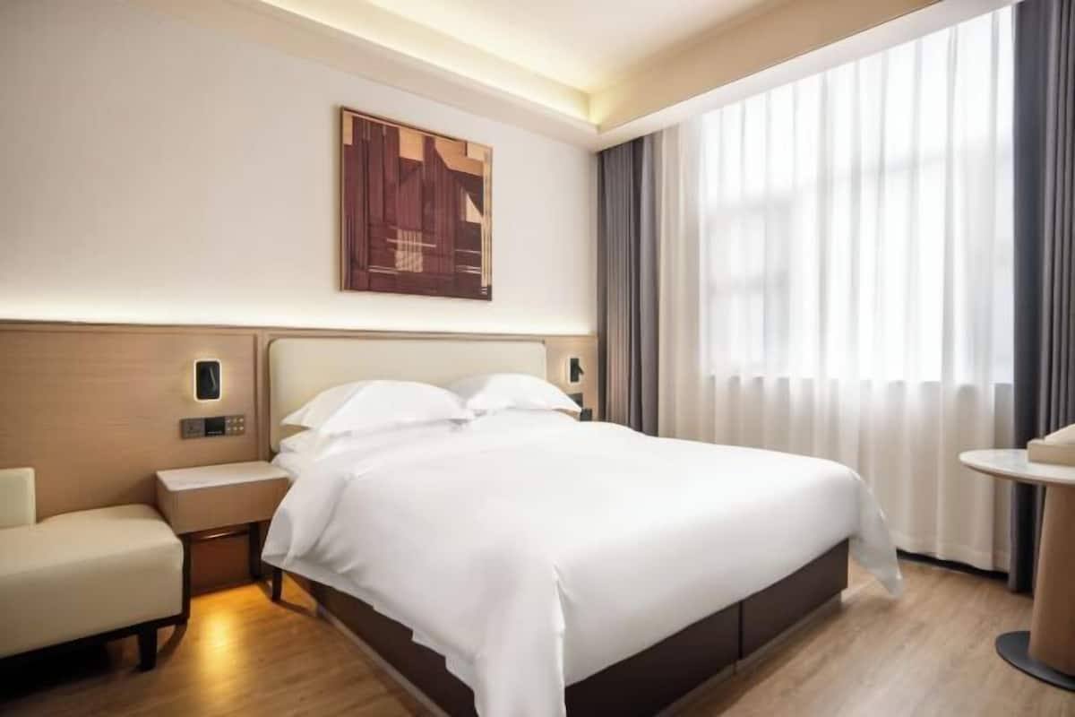Ein Hotelzimmer mit einem großen Bett, Nachttischen, einem Sessel, einem Schreibtisch und einem Fenster mit Vorhängen.