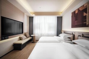 Ein Hotelzimmer mit Fernseher, zwei Betten, einer Couch, einem kleinen Tisch und einem großen Fenster mit Vorhängen.