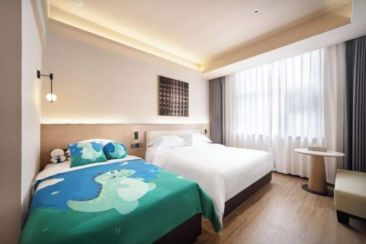Ein Hotelzimmer mit Bett, kleinem Tisch, Stuhl, Wandlampe und einem Fenster mit Vorhängen.