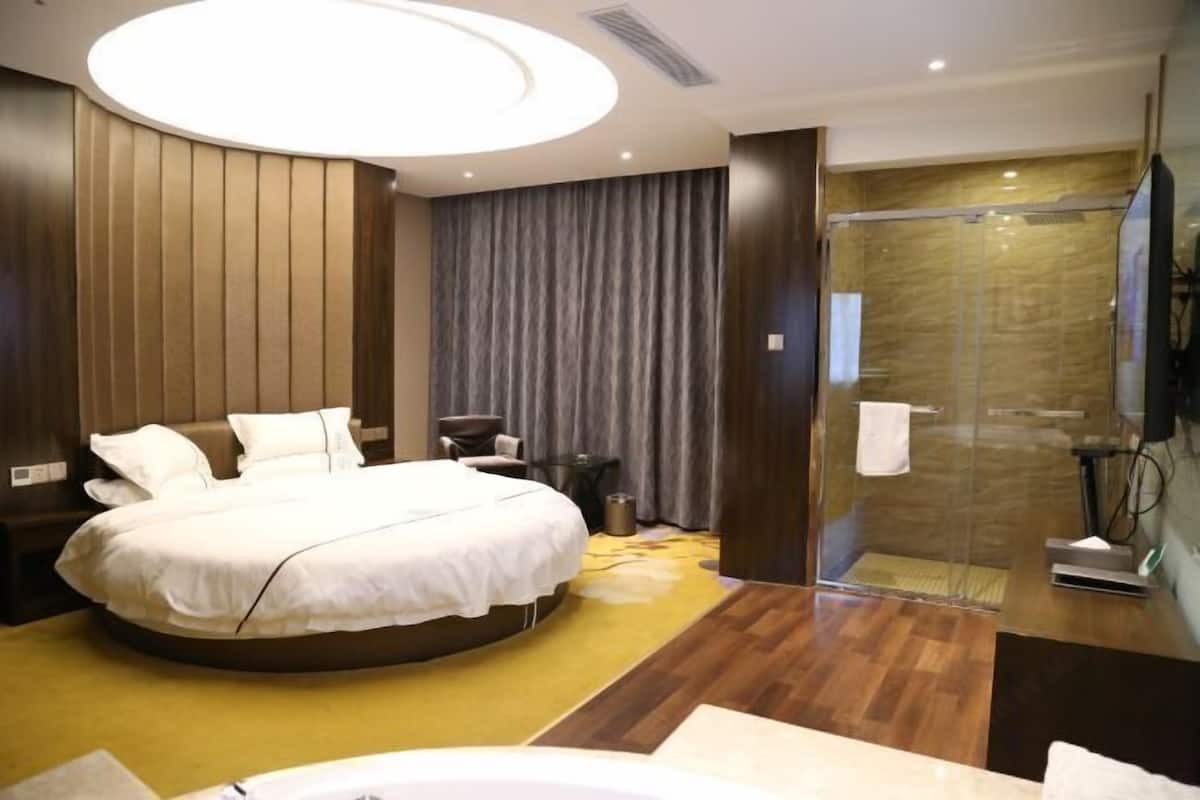 Ein modernes Hotelzimmer mit einem gebogenen Bett, einer in Glas eingefassten Dusche und Holzboden.