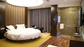 A modern hotel room with a curved bed, a glass-enclosed shower, and a wooden floor.