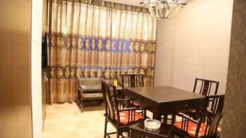 A dining area with a dark wooden table and chairs, a chandelier, and patterned curtains.