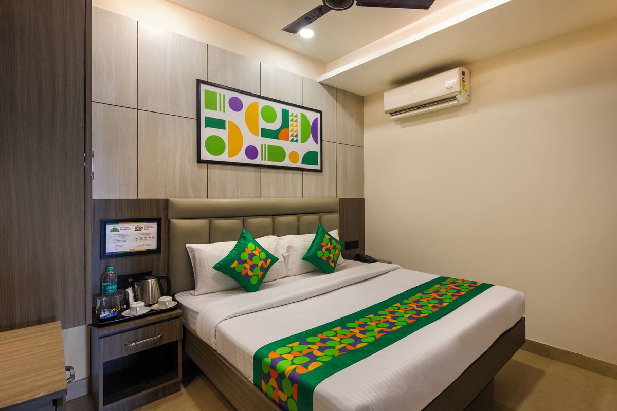 A hotel room with a bed, a nightstand, a coffee maker, a framed menu, and an air conditioning unit.