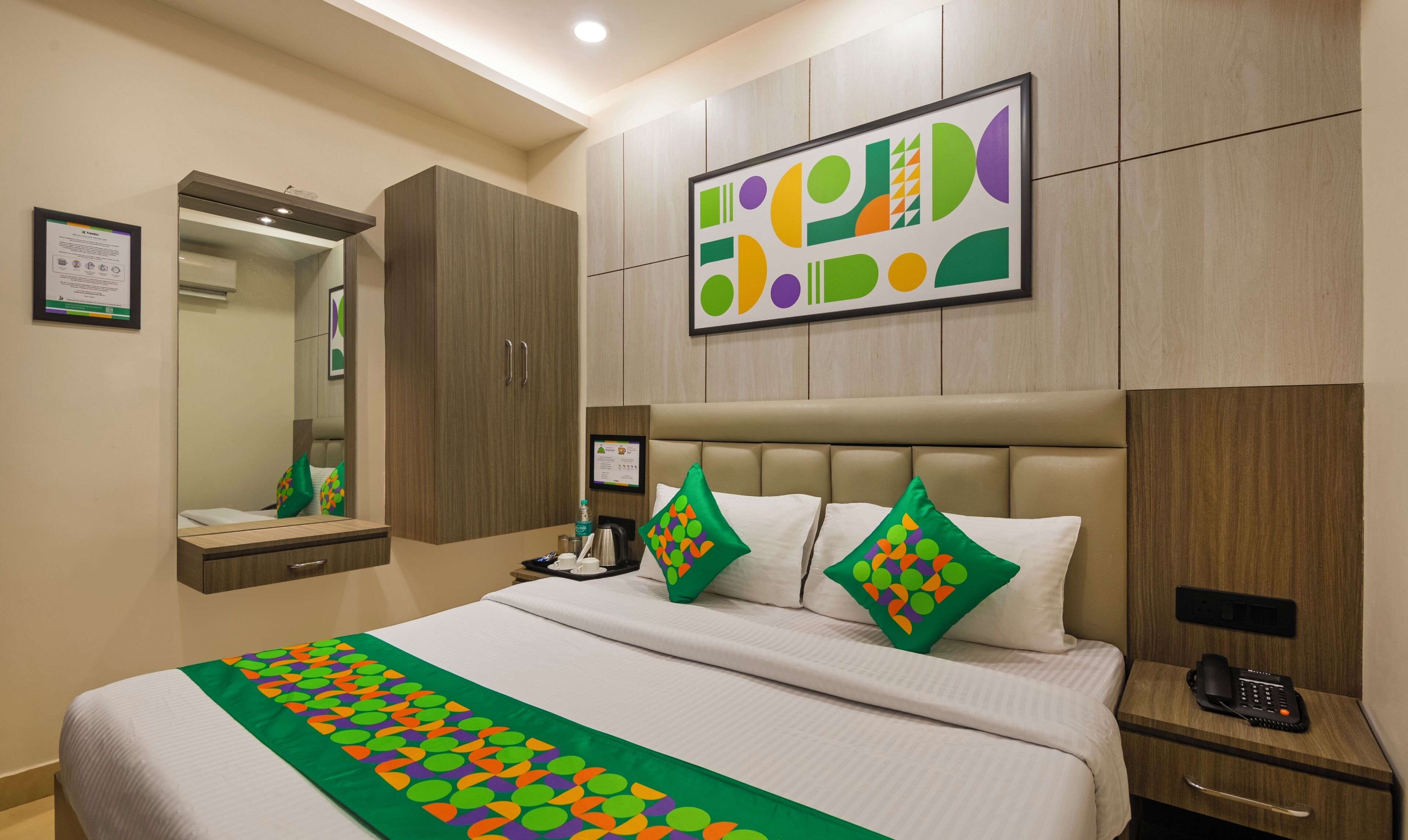 A hotel room with a large bed, a headboard, a bedside table with a phone, and a mirror.