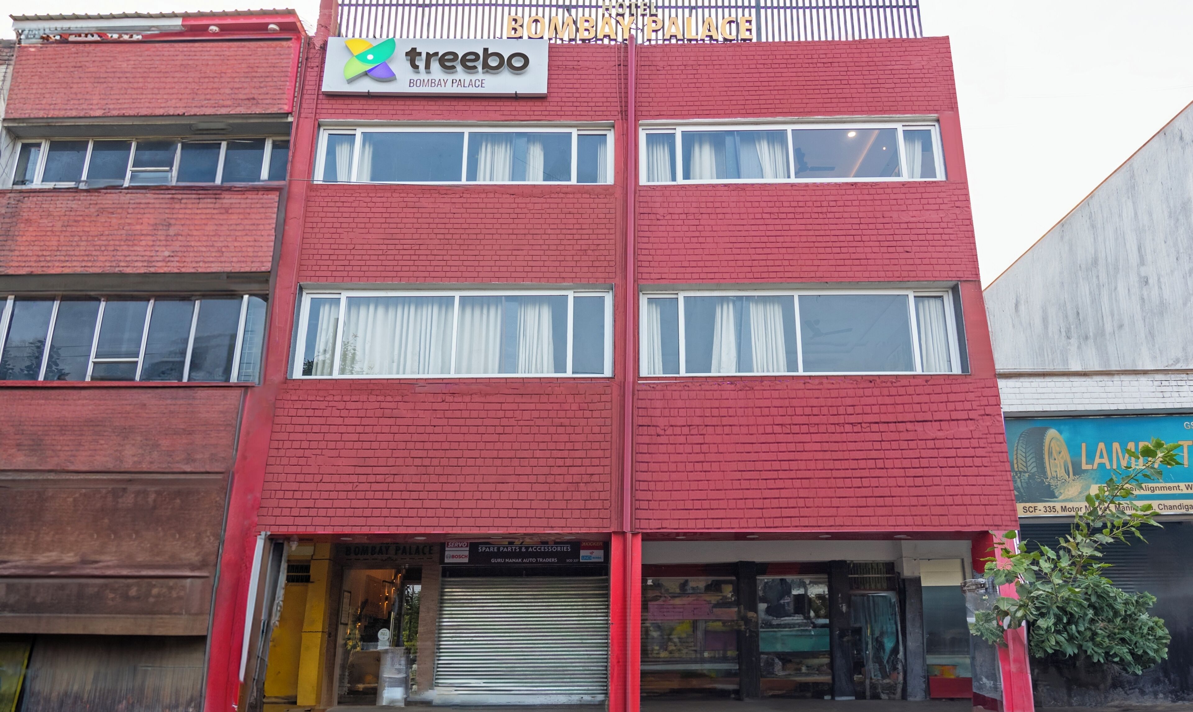 A red-brick building with a sign for 'Treebo' and 'Bombay Palace' hotel.