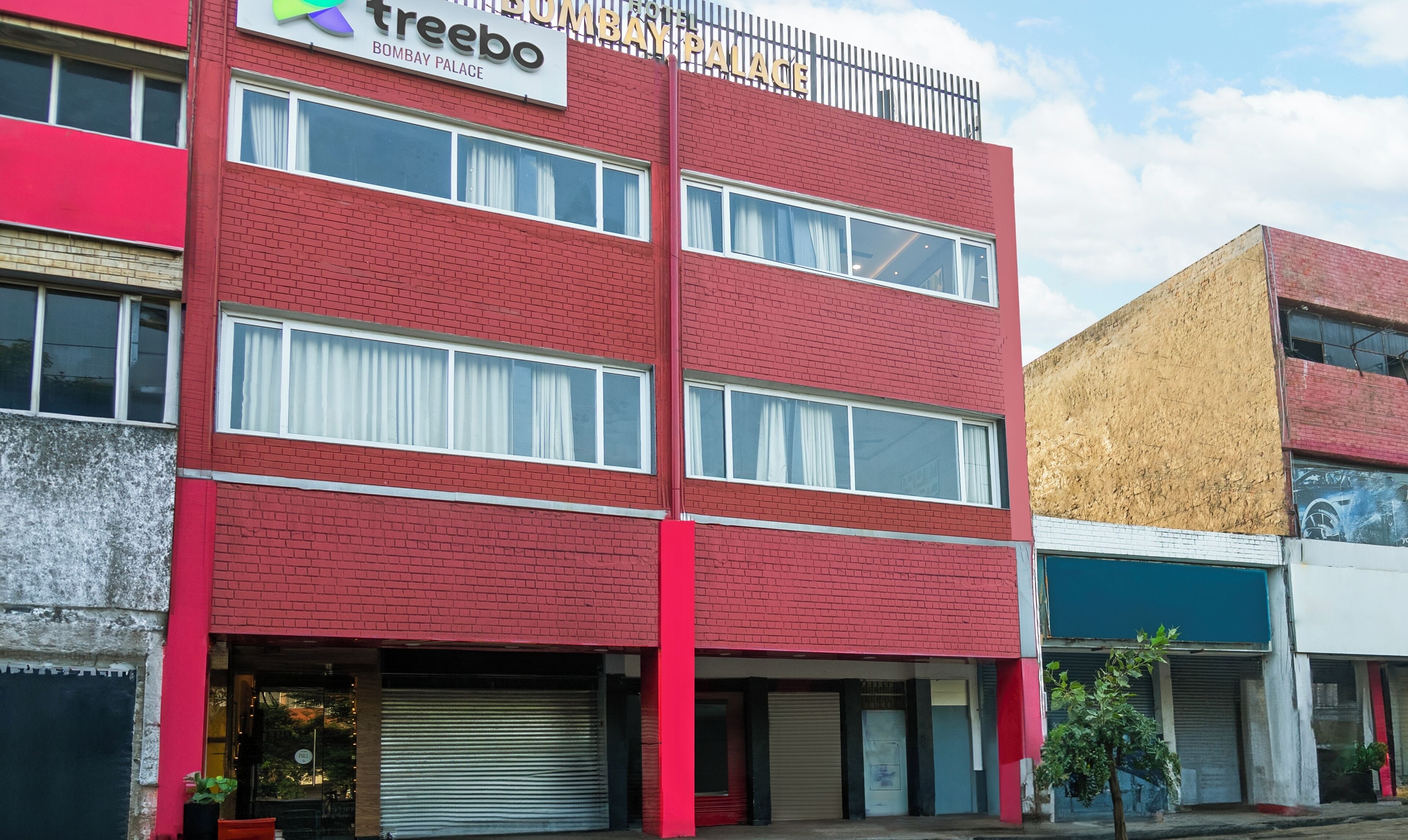 A red-brick building with a sign for 'Treebo Bombay Palace Hotel'.