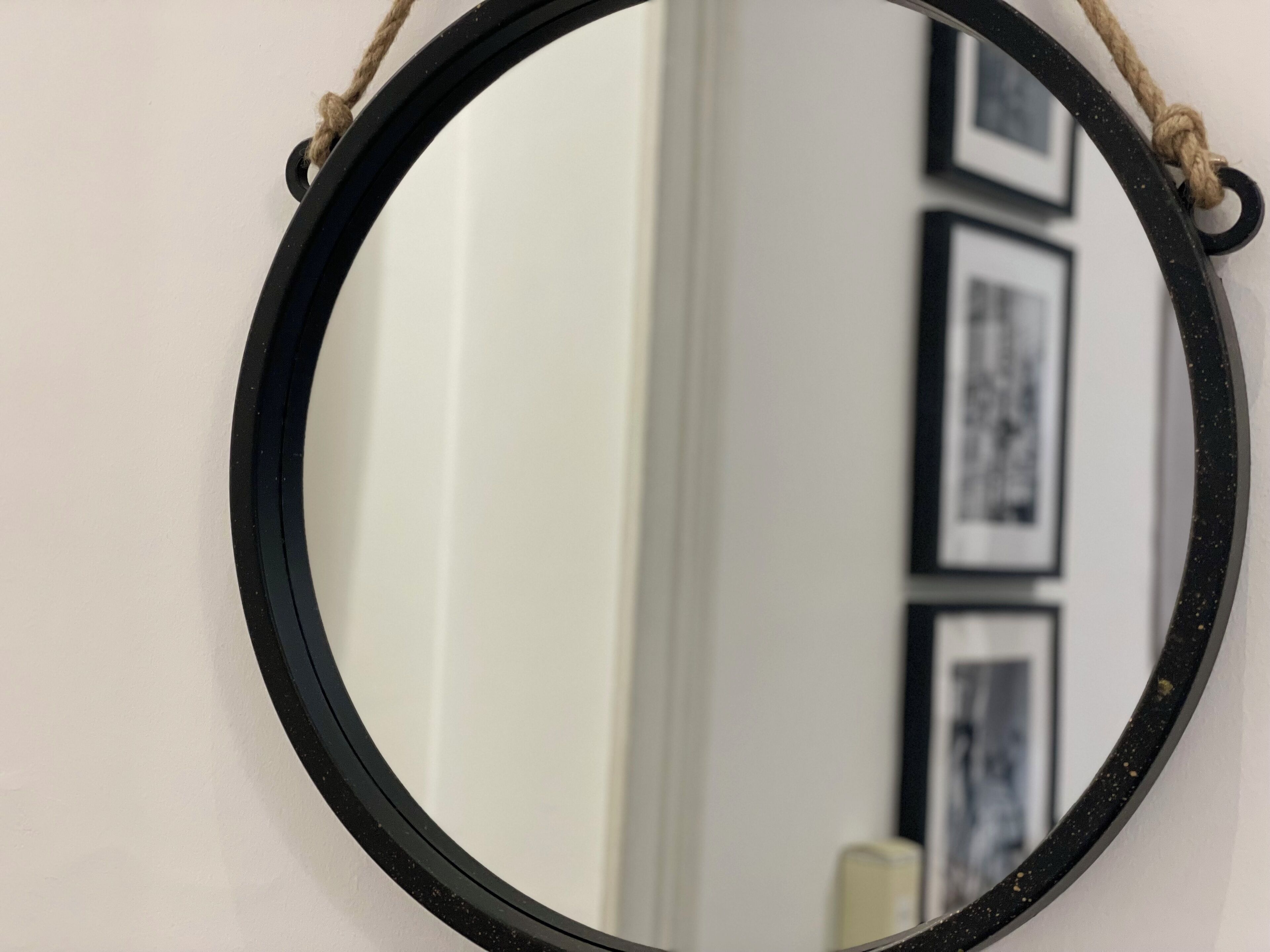 Un miroir rond, doté d’un cadre noir, est accroché à un mur blanc.