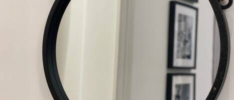 Un miroir rond, doté d’un cadre noir, est accroché à un mur blanc.