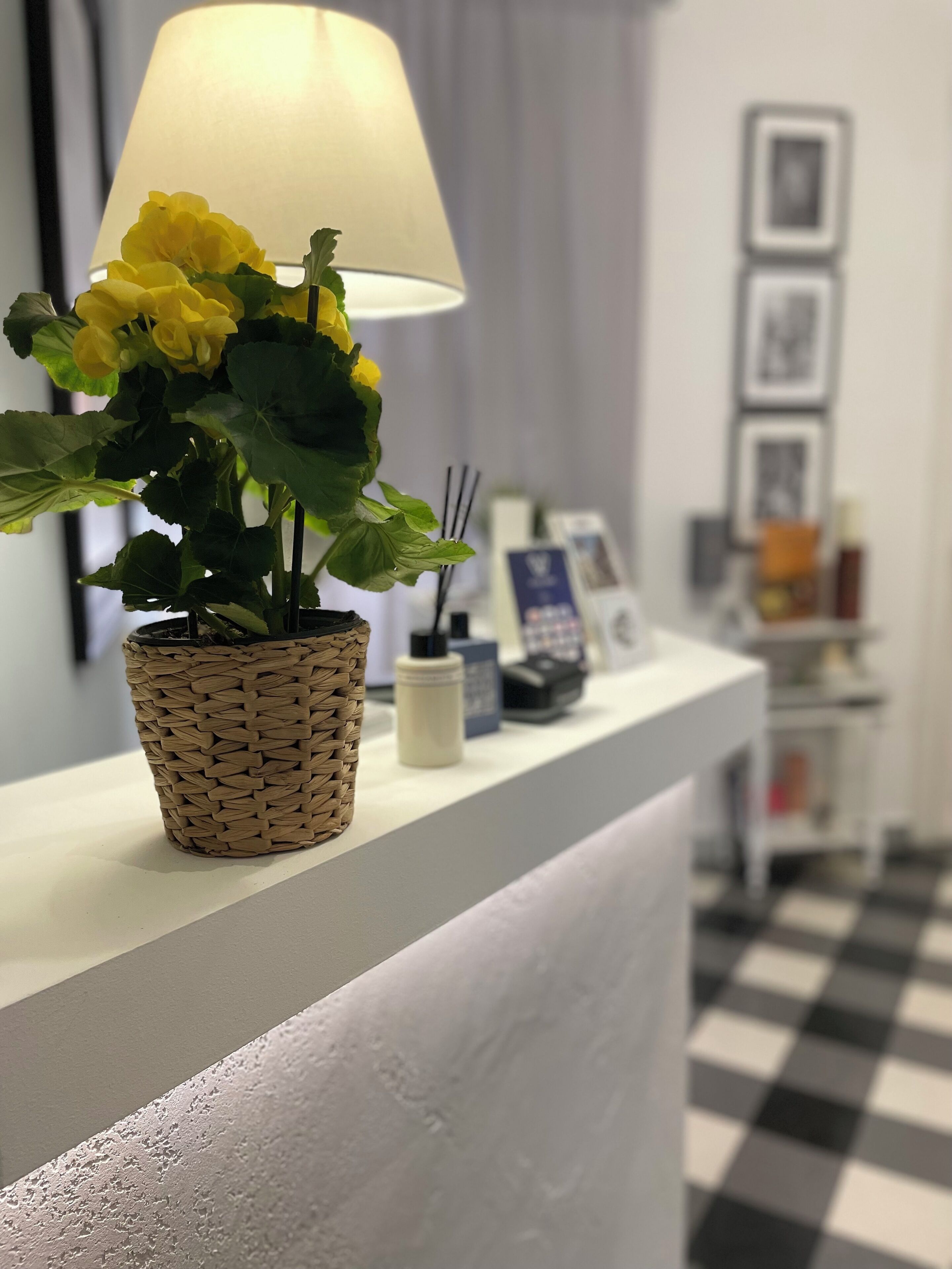 A reception desk with a woven basket holding yellow flowers, a lamp, and a small bottle, likely for hand sanitizer.