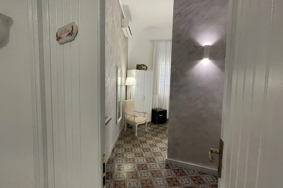 A hallway with a patterned floor, a white door, a small table with a lamp, and a chair.