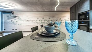 Une cuisine moderne avec une table à manger dressée pour deux personnes, agrémentée d’un ensemble de verres bleus et d’un couteau posé sur une serviette noire.