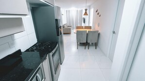 A modern kitchen with a stove, oven, and a dining area with a table and chairs. - Aquarius Residence (Fortaleza)