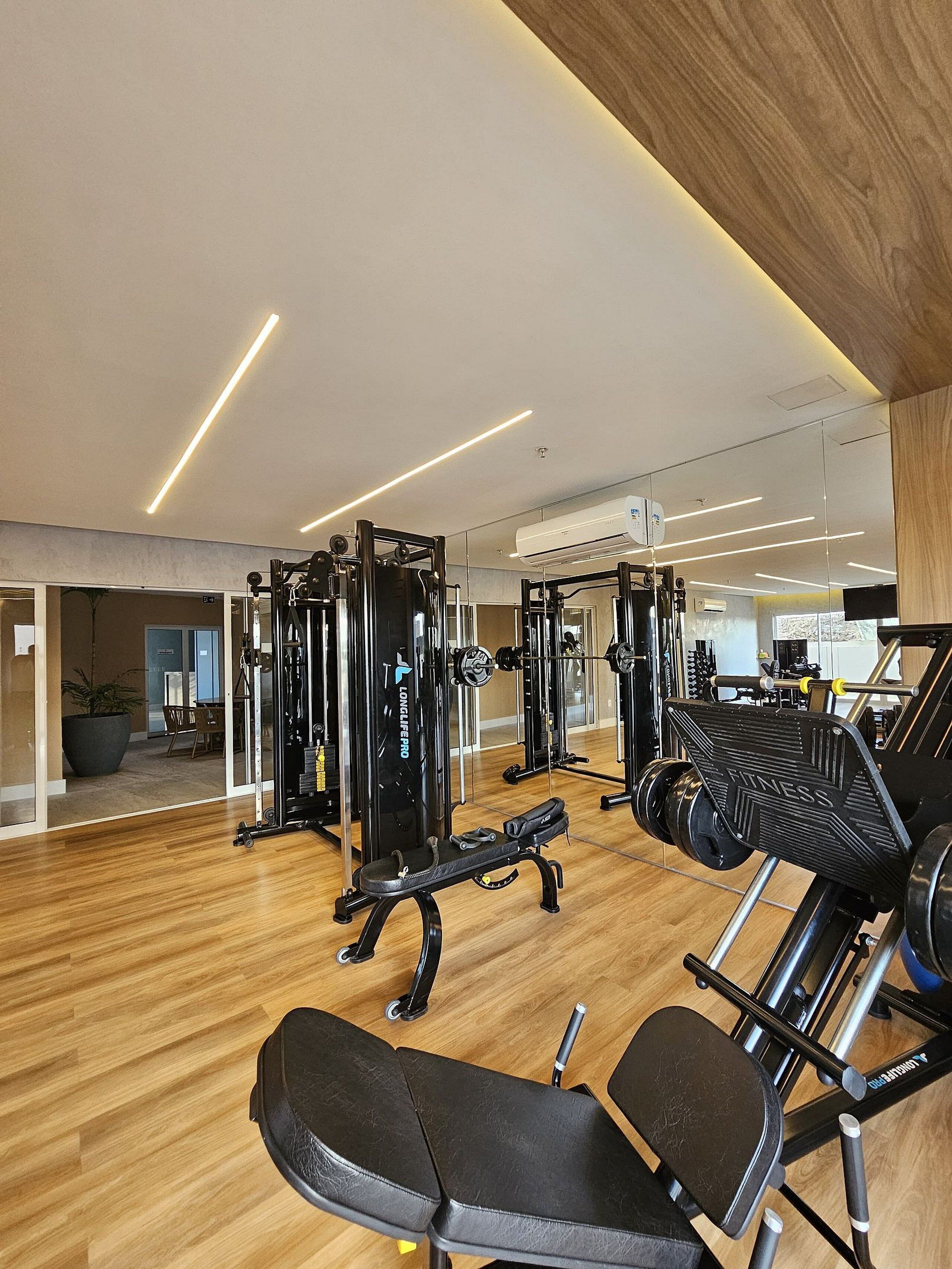 Een moderne sportschool met diverse fitnessapparaten, een houten vloer en een grote spiegel.