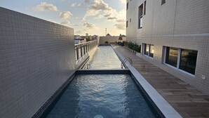 A swimming pool with a tiled deck, surrounded by a high-rise building with multiple windows. - Aquarius Residence (Fortaleza)