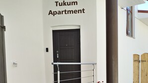 Eingang des Tukum Apartment mit einer schwarzen Tür, einem Metallgeländer und Blumentöpfen auf den Stufen.
