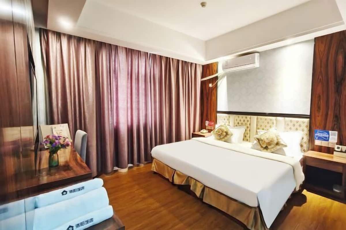 Habitación de hotel con cama, cortinas, un escritorio con silla, unidad de aire acondicionado y piso de madera.