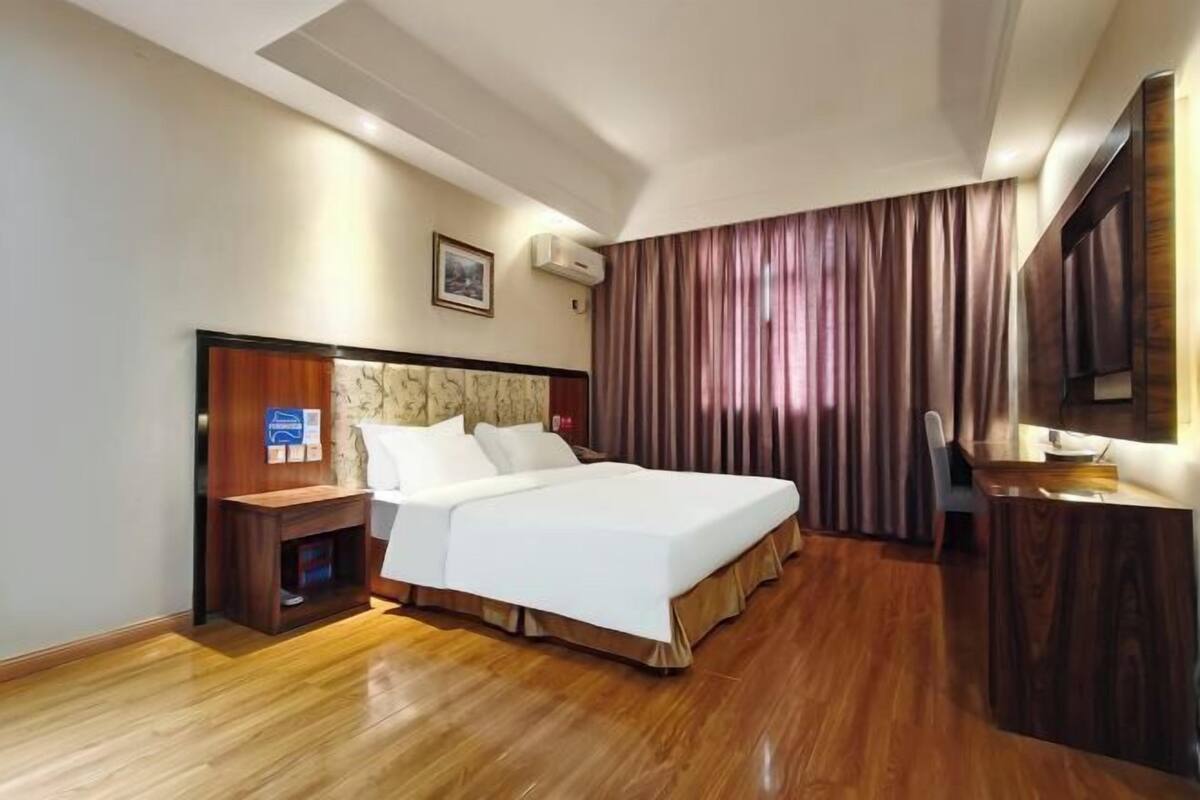 Una habitación de hotel con una cama grande, una mesita de noche de madera, un escritorio y un espejo.