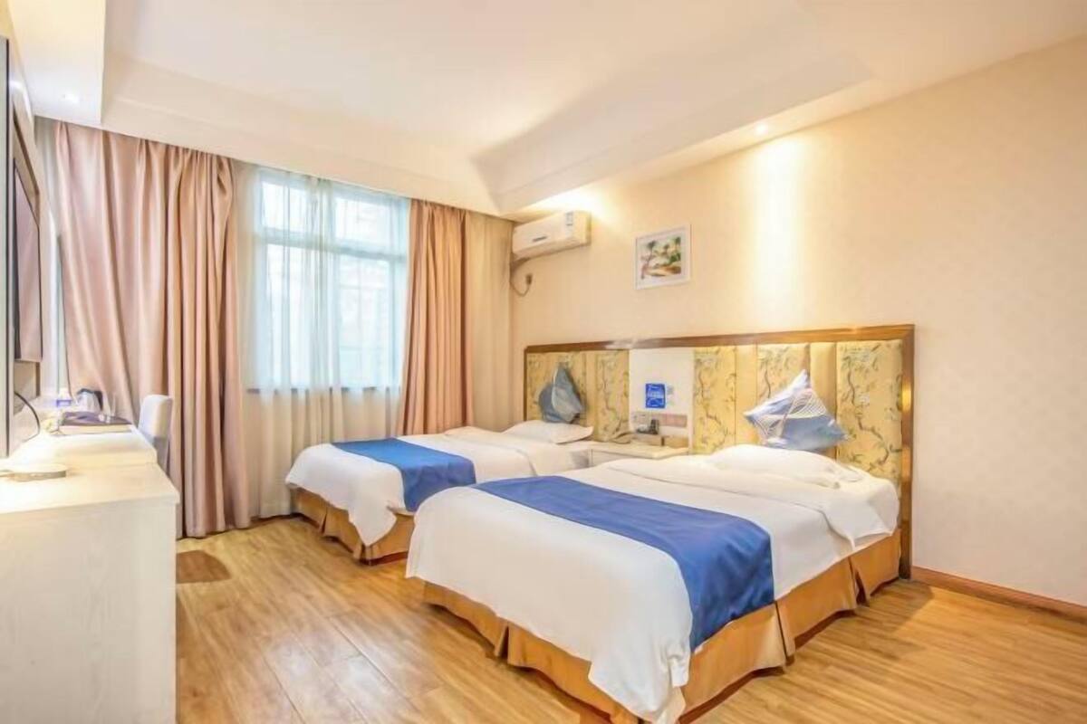 Habitación de hotel con dos camas, un escritorio y una ventana con cortinas.
