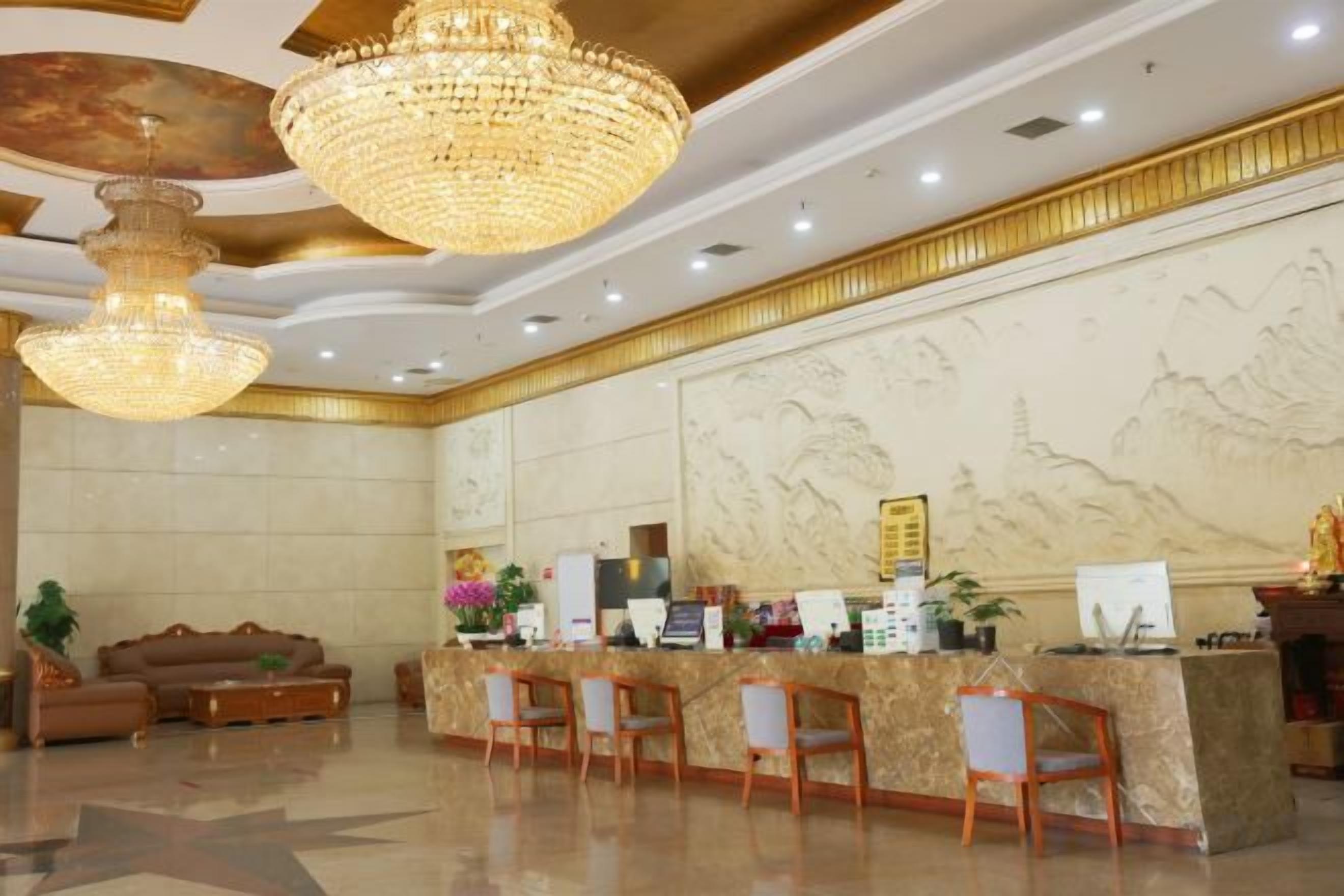 A hotel lobby with a reception desk, seating area, and chandeliers.
