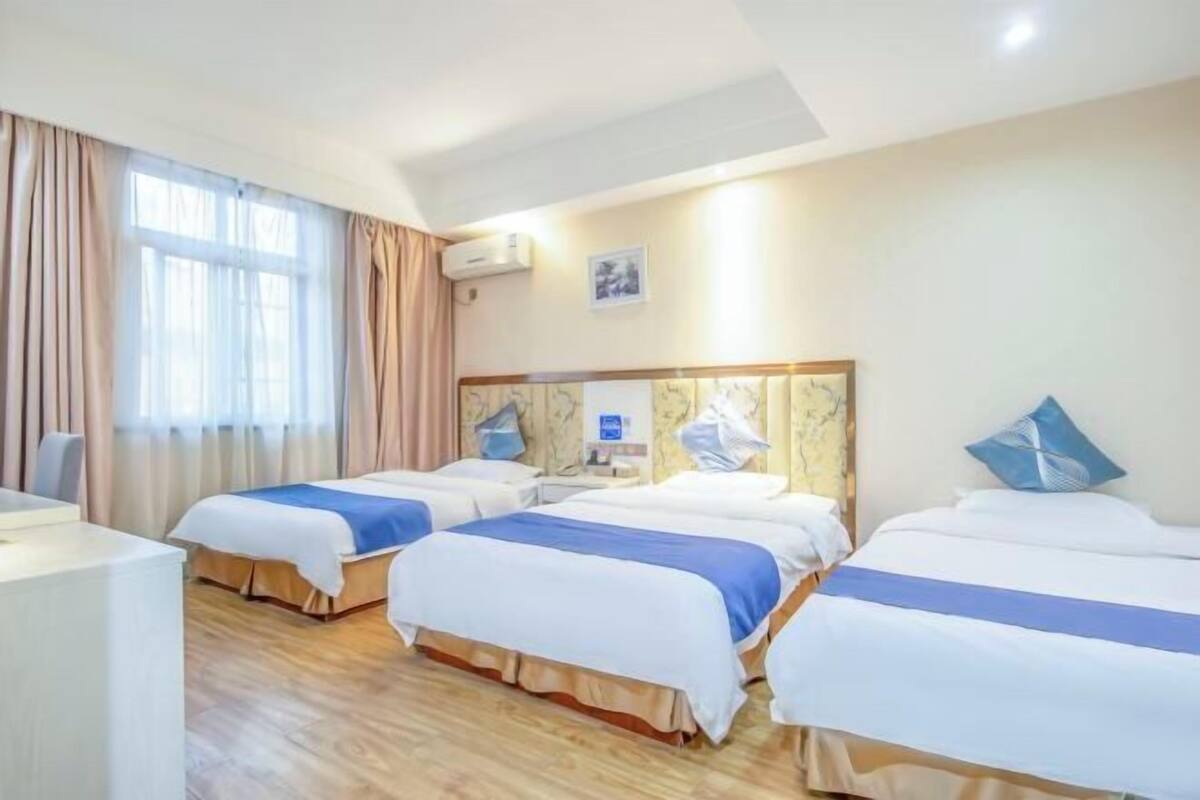 Una habitación de hotel con tres camas, un escritorio y un ventanal con cortinas.
