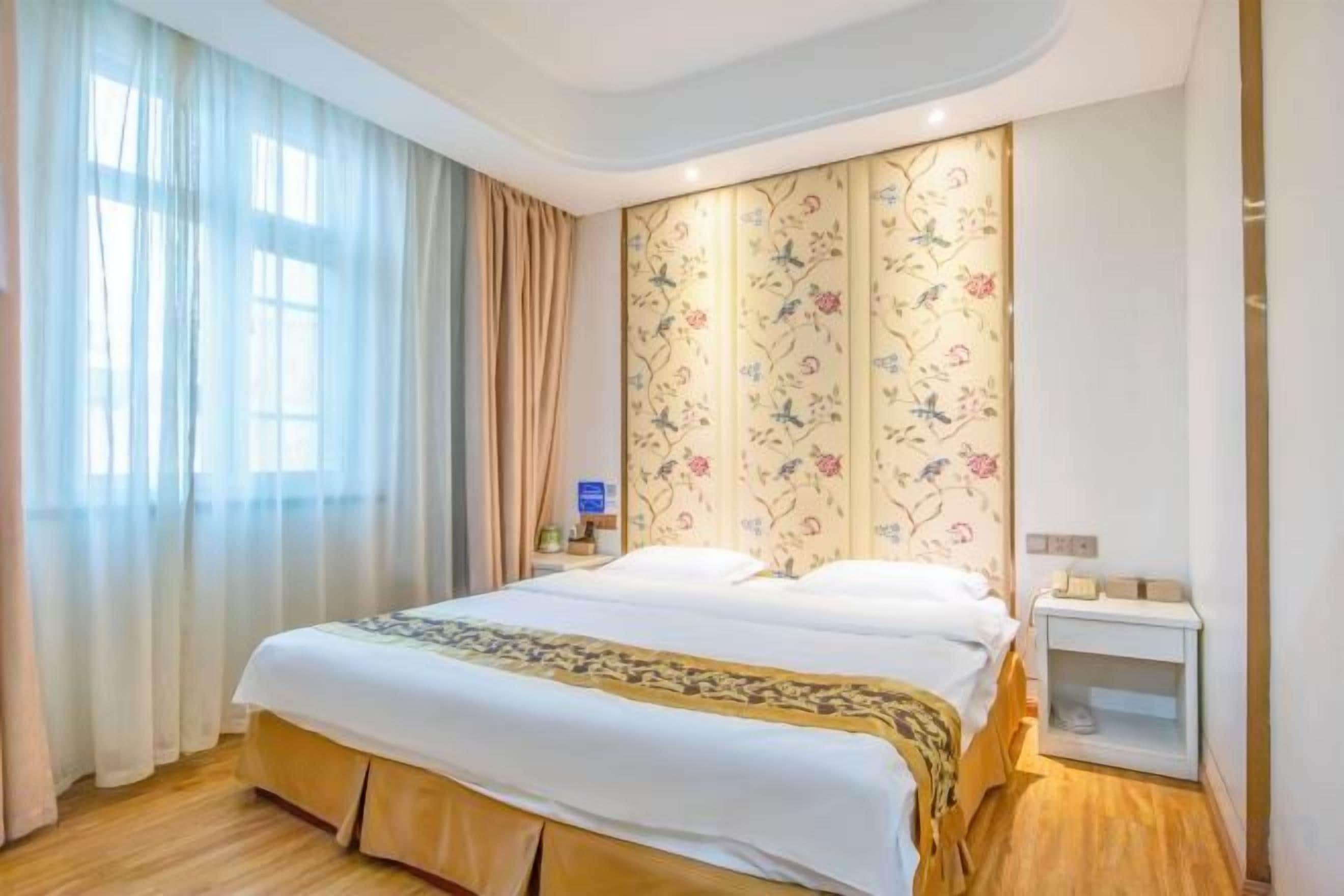 A hotel room with a large bed, a nightstand, and a window with curtains.