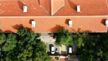 Vista aérea de un edificio con techo de tejas rojas, un área de estacionamiento y árboles en primer plano.