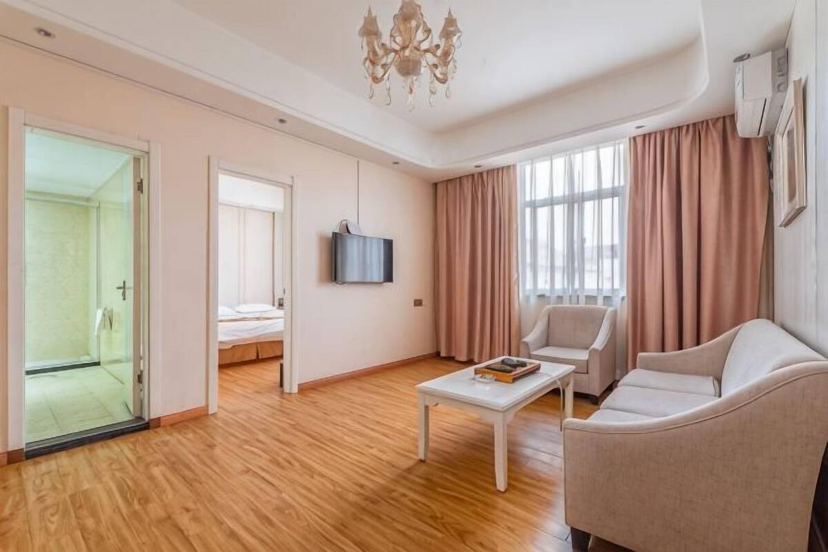 Una sala moderna con sofá, mesa de centro, televisor y puerta de vidrio que da a un dormitorio.