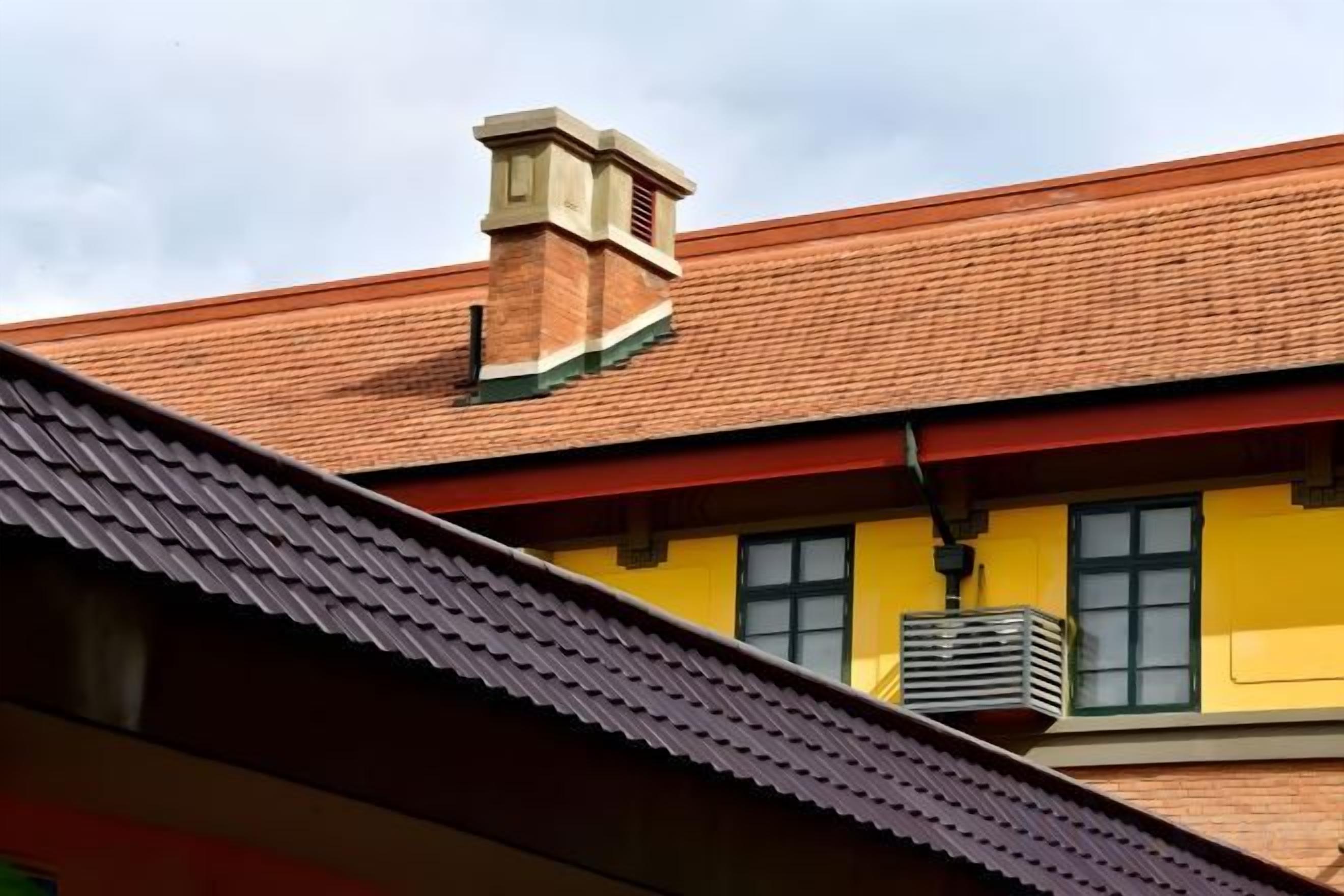 A building with a red-tiled roof, a visible chimney, and a yellow facade.