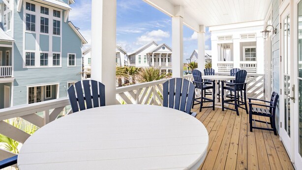 A covered outdoor deck with a round table and chairs, overlooking a coastal residential area. - 24/7 Barefoot Bliss 247 LAK (Port Aransas)
