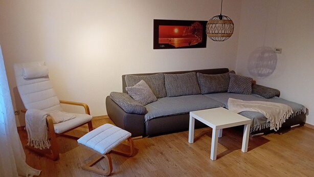 En stue med en grå sofa, en hvid lænestol, et lille hvidt bord og trægulv.