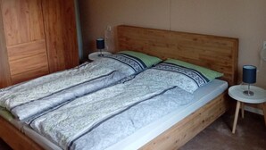 Et soveværelse med sengegavl i træ, et grønt og hvidt sengetæppe, to puder, et natbord med lampe og et træskab.