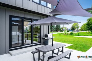 An outdoor patio with a grill, a table, and a large umbrella. - Wild Goose Landing- Located near local wineries and breweries (Kingsville)