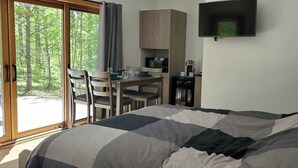 A bedroom with a bed, a desk, and a chair. There is a window with curtains, a flat-screen TV mounted on the wall, and a lamp on the side table. - Expedition Inn (Calumet)