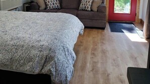 A bedroom with a bed, a sofa, a lamp, and a door leading to a balcony.
