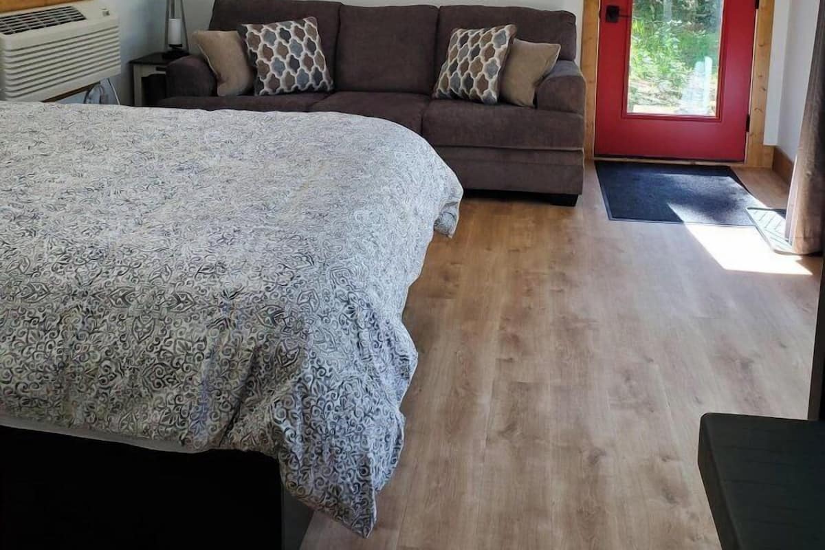 A bedroom with a bed, a sofa, a lamp, and a door leading to a balcony.