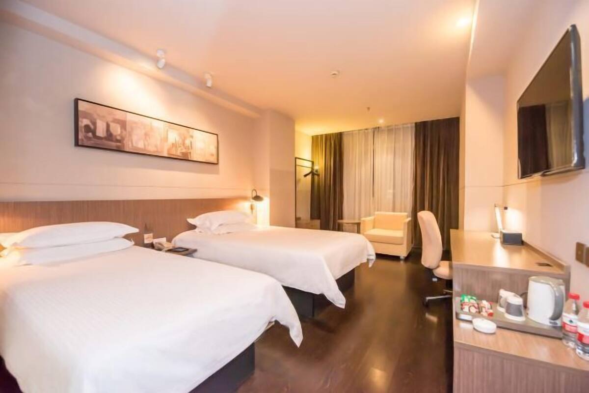 A hotel room with two beds, a desk, a chair, a TV, and a painting on the wall.