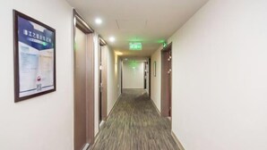 A hotel hallway with doors on both sides, a carpeted floor, and a green exit sign on the ceiling. - Jinjiang Inn Select (Foshan Guicheng Metro Station) (Foshan)