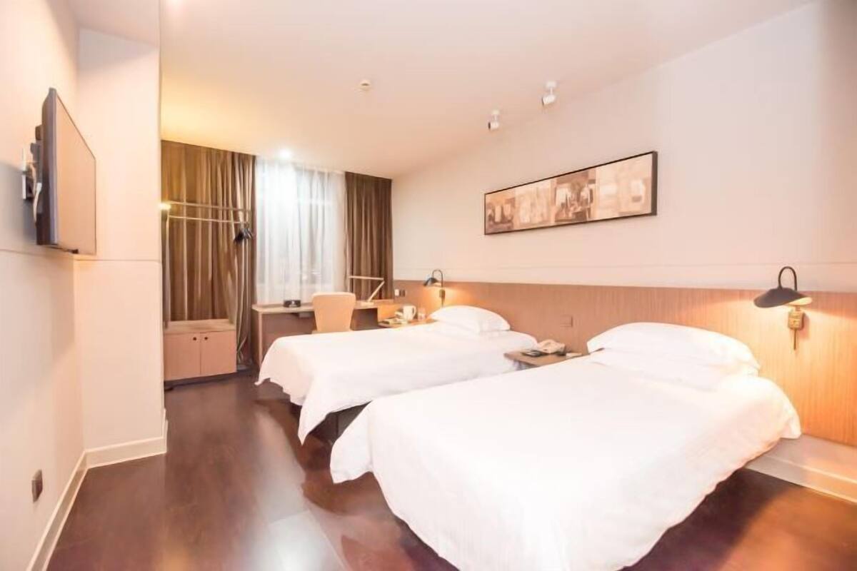 A hotel room with two beds, a television, a desk, and a window with curtains.