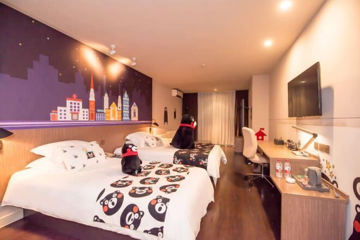 A hotel room with two beds, a desk, a chair, a TV, and a cityscape mural on the wall.
