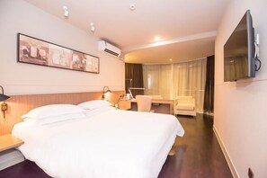 Quarto de hotel com uma cama grande, escrivaninha, cadeira, televisão e janela com cortinas.