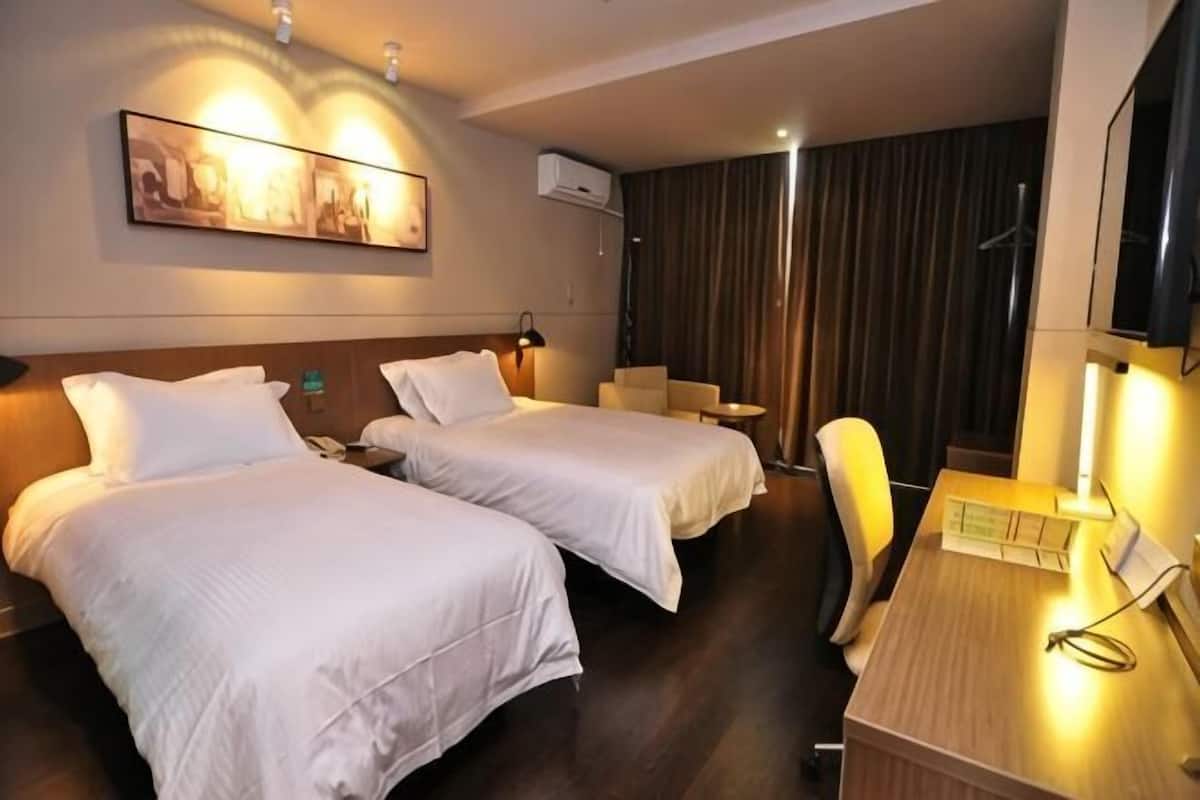 A hotel room with two beds, a desk, a chair, a TV, and a painting on the wall.