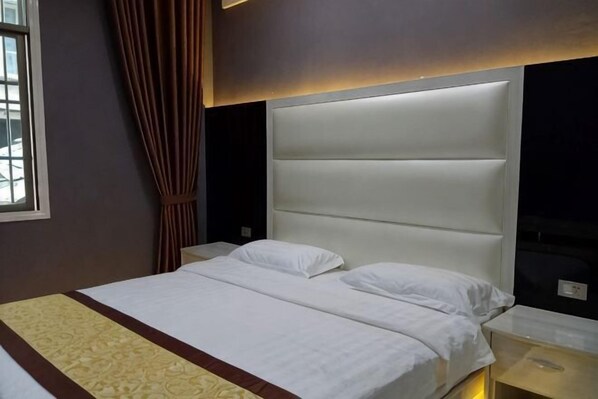 Une chambre d’hôtel avec un grand lit, une tête de lit, une table de chevet et une fenêtre avec des rideaux.