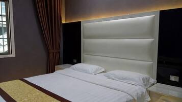 A hotel room with a large bed, a headboard, a bedside table, and a window with curtains.