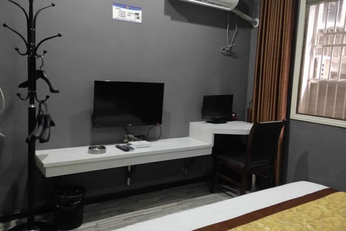 Ein Hotelzimmer mit weißem Schreibtisch, schwarzem Stuhl, Fernseher und einem Fenster mit Vorhängen.