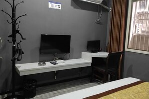 Habitación de hotel con un escritorio blanco, una silla negra, un televisor y una ventana con cortinas.