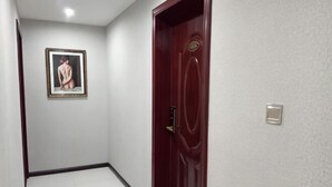 Un couloir avec une porte rouge, un tableau encadré au mur et un interrupteur.