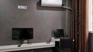 Une pièce avec un bureau blanc, deux écrans d’ordinateur, un climatiseur et une fenêtre avec des rideaux.