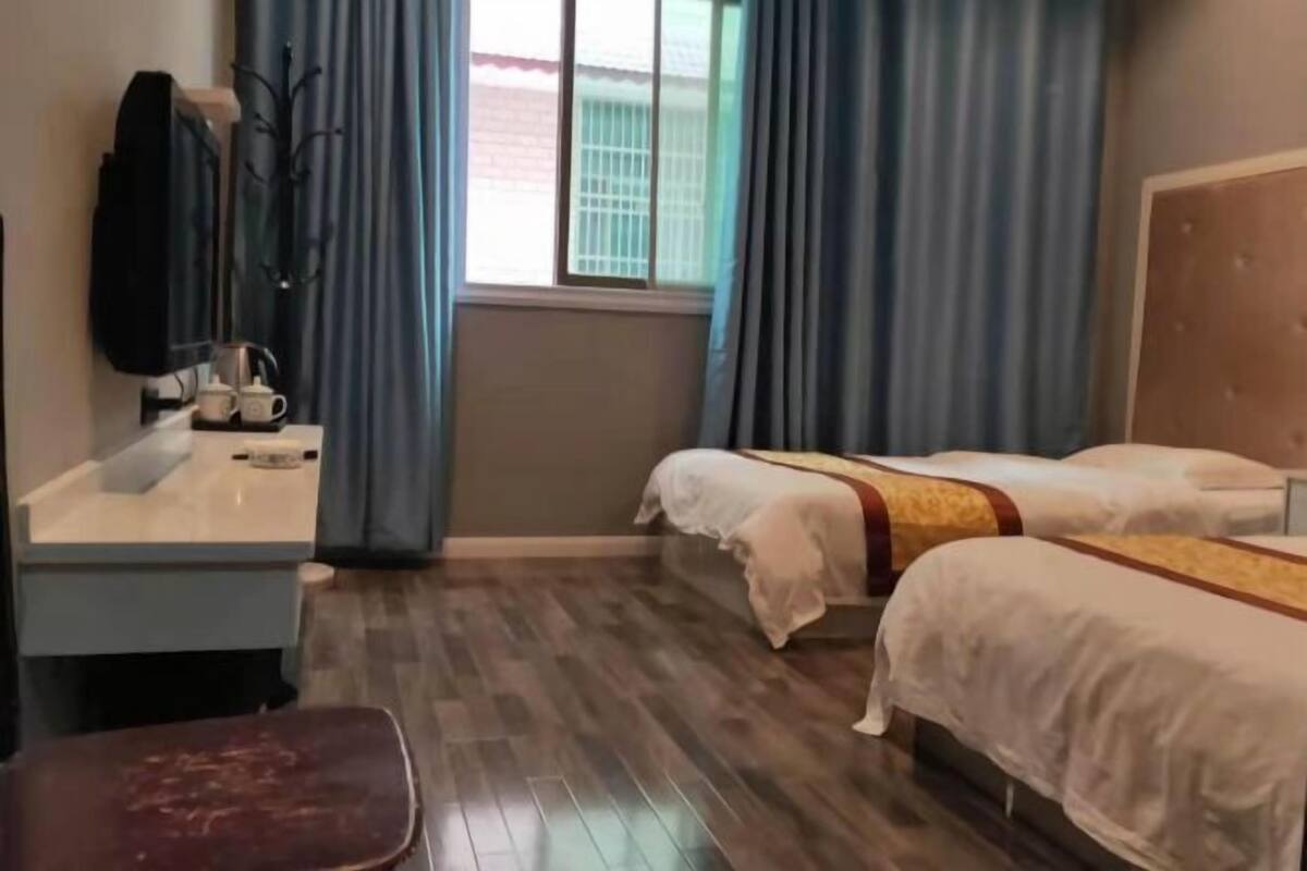 Ein Hotelzimmer mit zwei Betten, einem Schreibtisch mit Stuhl, einem Fenster mit Vorhängen und einem Kleiderständer.