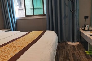 Una camera d'albergo con un letto, una finestra con tende, una scrivania con una lampada e un pavimento in legno.